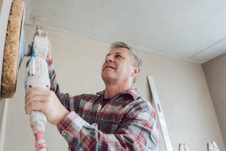 Plasterer smoothing interior wall of new homes with machineの写真素材