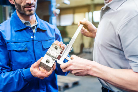 Two workers checking measurements of work piece in the factory being satisfiedの写真素材