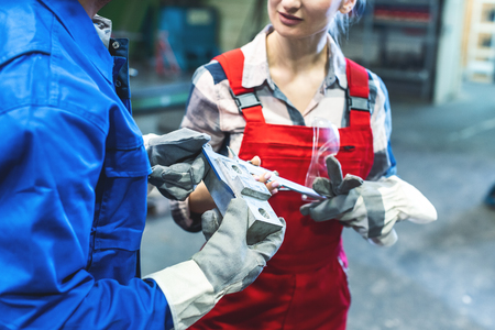Satisfied woman and man worker checking measurements of metal work pieceの写真素材