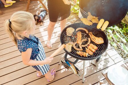 Little girl grilling the meat for the BBQ on a grillの写真素材