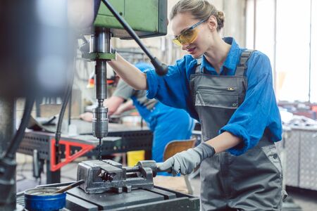 Metal worker woman operating drilling machine concentrating on her job