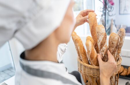 Baker woman putting French bread in a basket to sell it