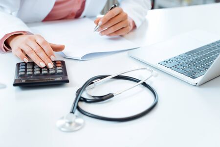 Closeup of doctor using calculator writing bills and doing bookkeepingの写真素材