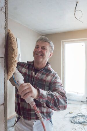 Plasterer man smoothing interior wall of new homes with machineの写真素材