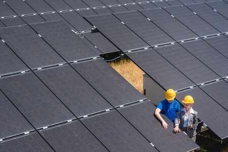 Two people standing amid solar cells in a power plant inspecting the modulesの写真素材