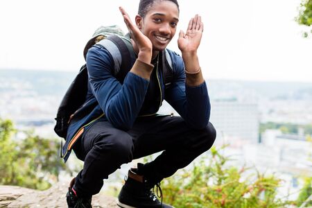 Smiling male hiker carrying his backpack crouchingの写真素材