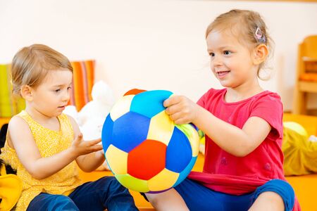 Two girls in play school having fun with a colorful ballの写真素材