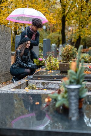 Couple in grief on a cemetery in fall while it is rainingの写真素材