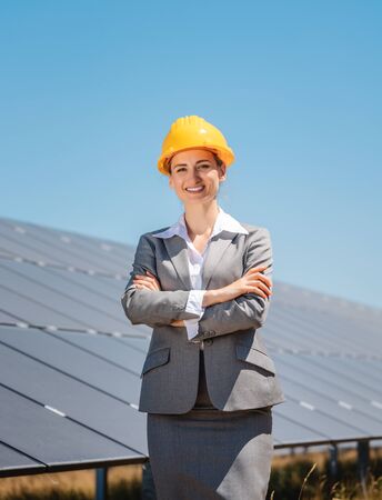 Woman investor in clean energy standing proudly in front of solar panelsの写真素材