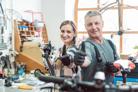 Two bike mechanics in their workshop having a successful day showing their thumbs