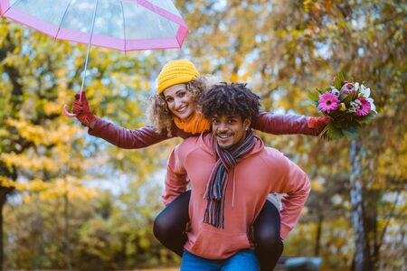 Black man carrying his Caucasian girl piggyback in fall both being joyfulの写真素材