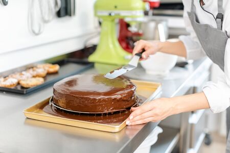 Patissier pouring liquid chocolate on a cake in her workshop