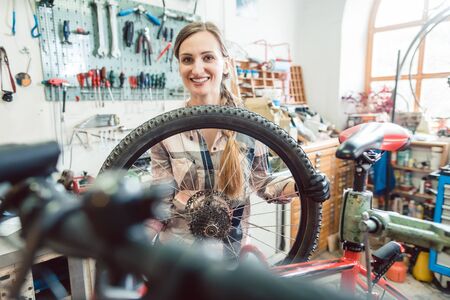 Very happy bike mechanic woman looking through the wheel of bicycleの写真素材