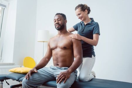 Physical therapist massaging a young black man on shoulder after a sport injuryの写真素材