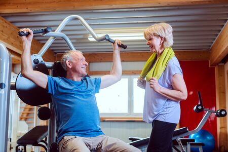 Happy senior man in the gym with his wife on exercise machines