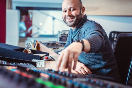 Sound engineer mixing a song in his studio pushing a fader and the console up