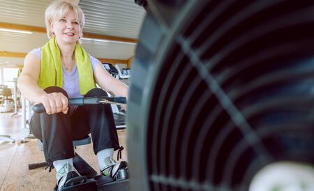 Healthy senior woman on the rowing machine in a fitness gym