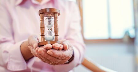 Senior in nursing home holding a hourglass - time is running up quickly