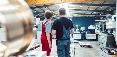 Workers on the metalworking factory floor discussing the next project