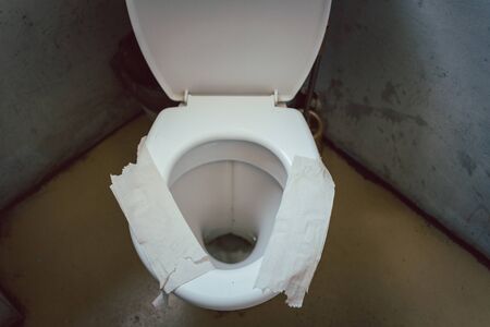 Filthy toilet seat covered with toilet paper as improvised sit down insulationの写真素材