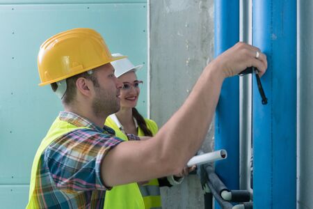 Construction workers measuring pipes on site with tape
