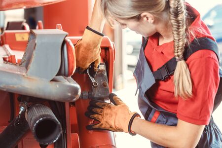 Woman machinist working with wrench of a farm machine doing some fixing or maintenanceの写真素材