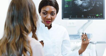 Black gynecologist showing woman early ultrasounds of her pregnancyの写真素材