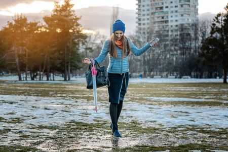 Woman having a city walk in thawing snow avoiding the puddles