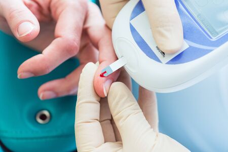 Nurse testing blood sugar level of woman for diabetes with tool with test strip