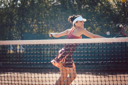 Woman in red sport dress playing tennis hitting the ballの写真素材