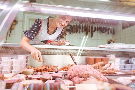 Saleswoman in butchery behind glass display with traditional meat and sausagesの写真素材