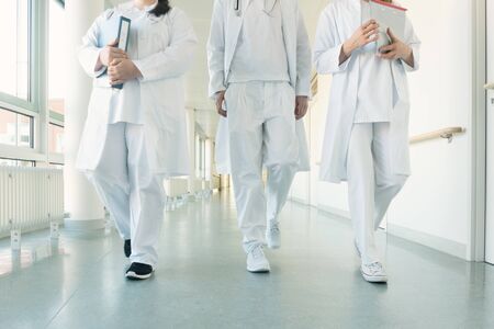 Doctors, two women and a man, in hospital walking down the corridorの写真素材