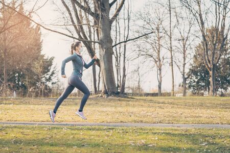 Fit woman running during health crisis with face mask jogging down a pathの写真素材