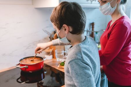 Mother and son cooking at home together wearing masks in the kitchenの写真素材