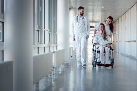 Doctor, nurse, and patient in wheelchair walking on hospital corridorの写真素材