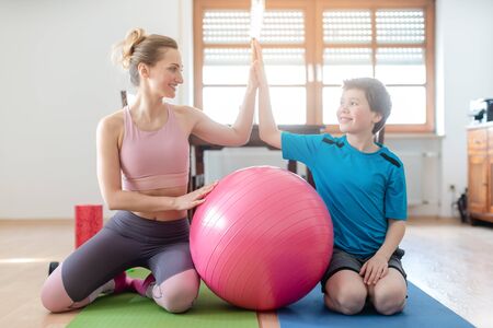 Mother and son giving each other a high-five after fitness exercise at home with pink ballの写真素材