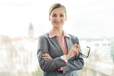 Business woman wearing sharp suit in her office standing by the windowの写真素材