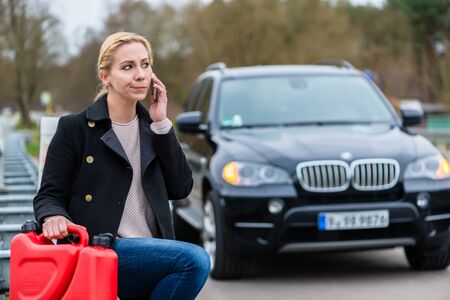 Woman has car with empty gas tank calling for help on phone holding spare canister in handの写真素材