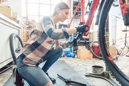 Happy woman working as a bicycle mechanic servicing a bikeの写真素材