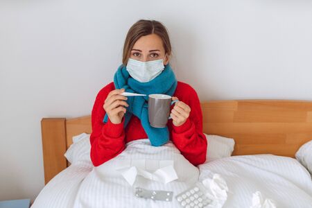 Woman contracted Covid-19 measuring fever in bed looking worried at thermometerの写真素材
