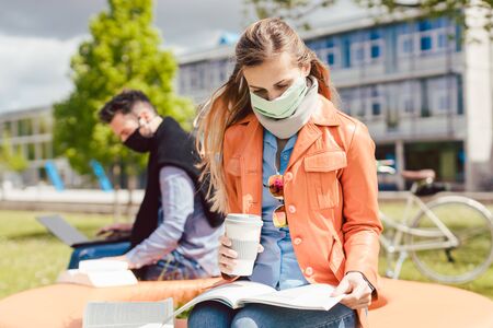 Man and woman practicing social distancing in university while learning and reading