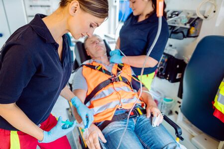 Emergency doctor woman giving drop injection to injured man in ambulanceの写真素材