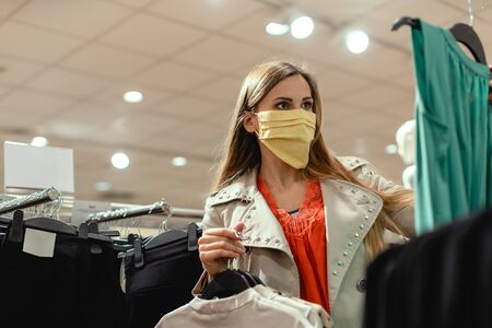 Woman shopping in fashion store wearing face mask looking at some clothes
