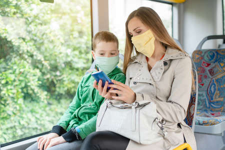 Woman with her son in the bus during coronavirus crisis looking at the phone