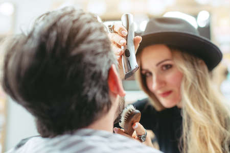Woman barber cutting and trimming beard of client in her shopの写真素材