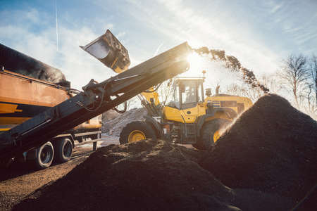 Heavy machinery moving earth and biomass in compost works or landfill