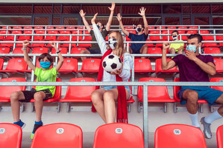Fans watching football match under social distancing measures in stadium wearing masks