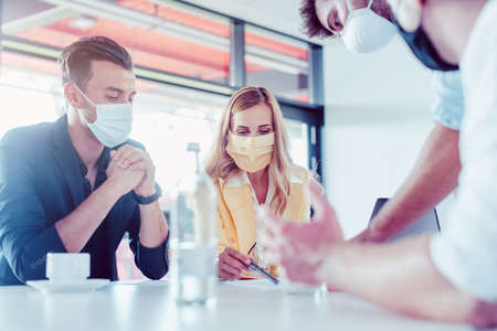 Team of business people with face masks during project meeting in Corona times