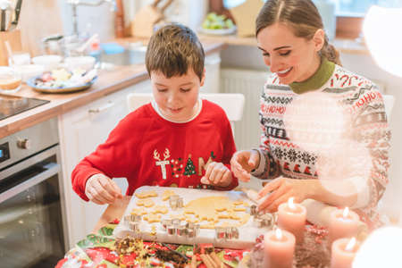 Mother and son decorating Christmas cookies on the sheet in the family kitchenの写真素材