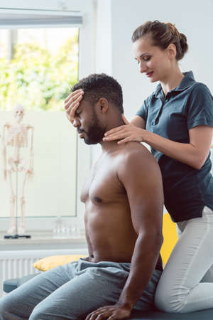 Woman physical therapist massaging young black man holding his headの写真素材